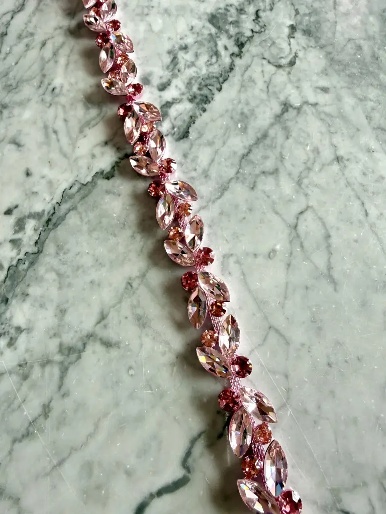 Galón de cristal delgado en tono rosa con diseño de hojas. Ideal para vestidos de gala, cinturones y alta costura. Compra por medio metro online.